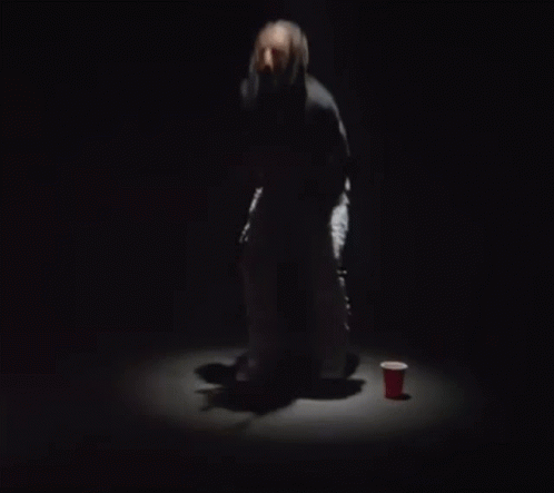 A Woman Is Dancing On A Stage In A Dark Room With A Microphone In Her Hand . GIF