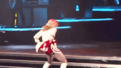 A Woman Is Dancing On A Stage Wearing A White Jacket And Boots . GIF