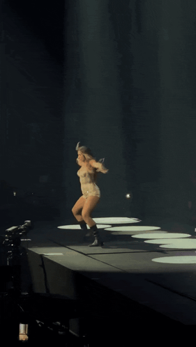 a woman is dancing on a stage with her arms outstretched in the dark