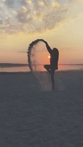 A Woman Is Dancing On The Beach At Sunset With Smoke Coming Out Of Her Feet GIF