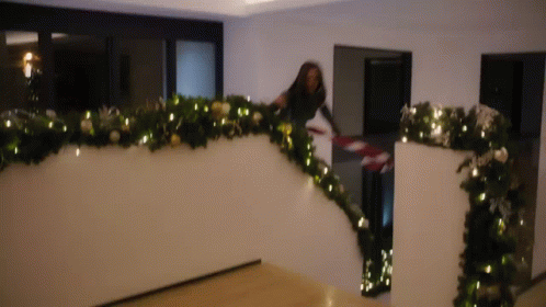 A Woman Is Decorating A Staircase With Christmas Decorations . GIF