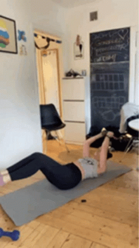 A Woman Is Doing A Crunch On A Yoga Mat In A Room . GIF