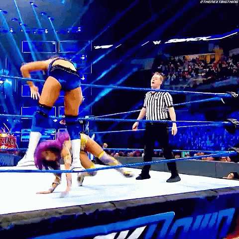 A Woman Is Doing A Handstand In A Wrestling Ring With A Referee Watching . GIF