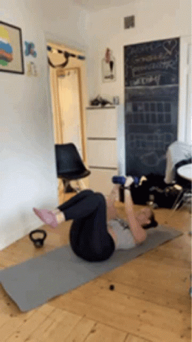 A Woman Is Doing Exercises On A Yoga Mat In A Living Room GIF