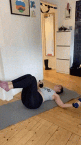 A Woman Is Doing Exercises On A Yoga Mat In A Room . GIF