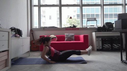 A Woman Is Doing Exercises On A Yoga Mat In Front Of A Red Couch With A Sign That Says " Do Not Enter " GIF