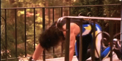 A Woman Is Doing Push Ups On A Balcony Next To A Fence . GIF