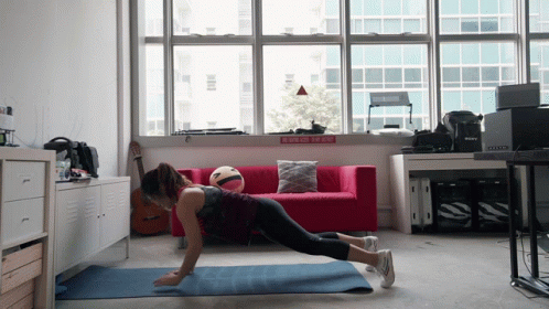 A Woman Is Doing Push Ups On A Yoga Mat In Front Of A Red Couch And A Sign That Says No Smoking GIF