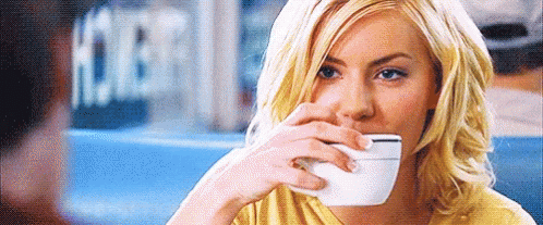 A Woman Is Drinking A Cup Of Coffee While Sitting At A Table In A Restaurant . GIF