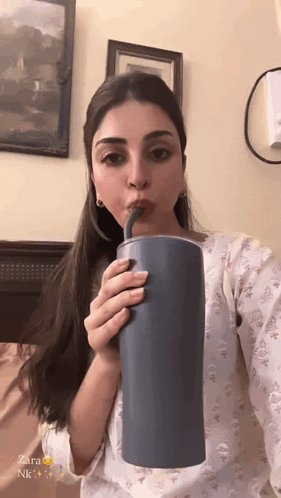 A Woman Is Drinking From A Blue Cup With A Straw And The Name Zara Is On The Bottom GIF