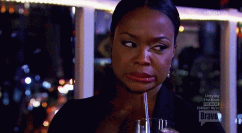 A Woman Is Drinking Through A Straw From A Glass And Making A Funny Face . GIF