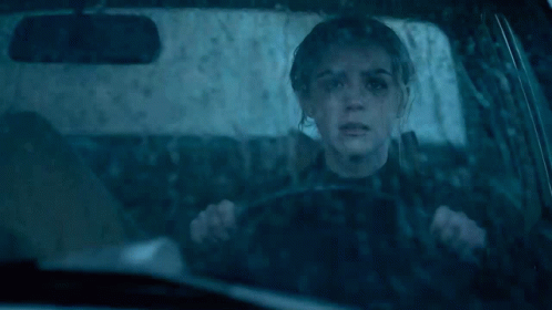 a woman is driving a car in the rain with a reflection of her face in the windshield