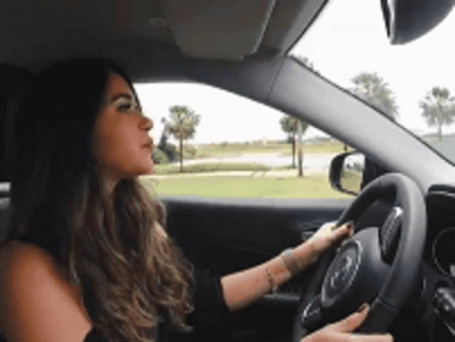 A Woman Is Driving A Car On A Road GIF