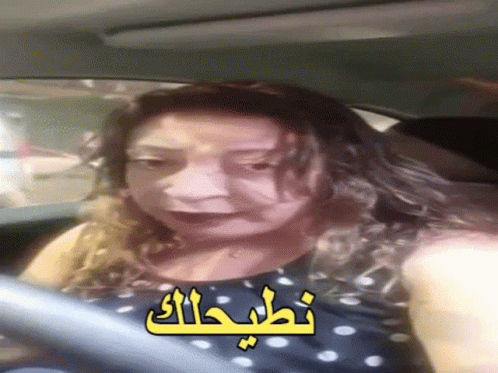 A Woman Is Driving A Car With Arabic Writing On The Side GIF