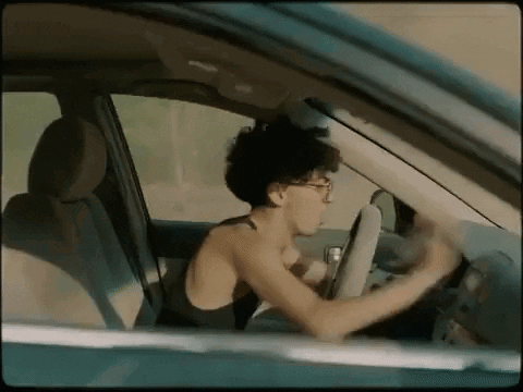 A Woman Is Driving A Car Without A Shirt On While Looking Out The Window . GIF