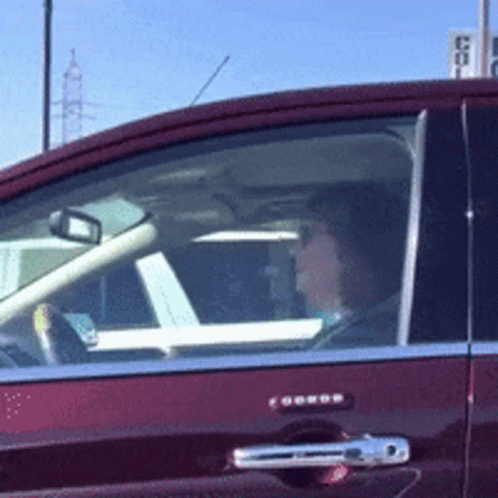 A Woman Is Driving A Red Car With A Sign In The Background That Says ' Coca Cola ' GIF