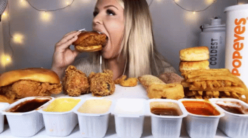 A Woman Is Eating A Chicken Sandwich In Front Of A Popeye Coldest Cup GIF