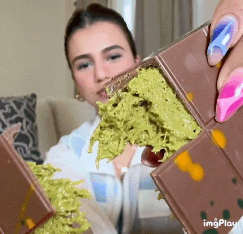 A Woman Is Eating A Chocolate Bar With Green Icing GIF