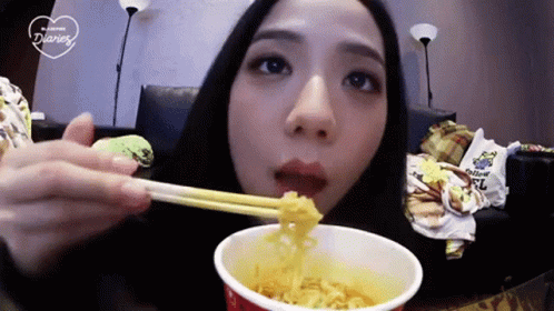 A Woman Is Eating A Cup Of Noodles With Chopsticks GIF
