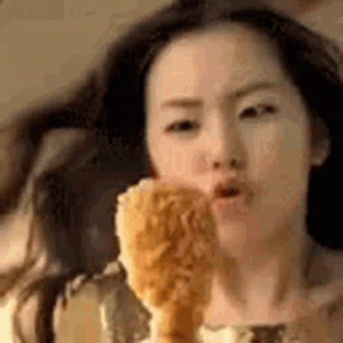 A Woman Is Eating A Fried Chicken Leg In A Close Up . GIF
