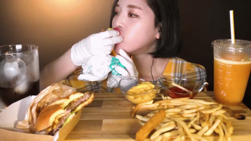 A Woman Is Eating A Hamburger And French Fries With A Drink That Says Purple GIF