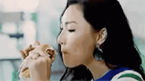 A Woman Is Eating A Hamburger In A Restaurant . GIF