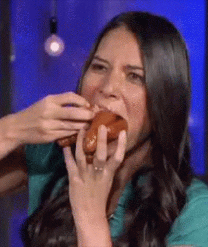 A Woman Is Eating A Hot Dog With Her Hands While Wearing A Ring . GIF