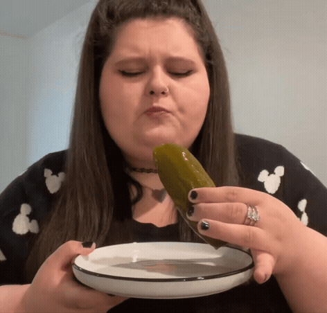 A Woman Is Eating A Pickle From A Plate With A Knife . GIF