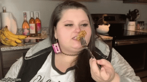 A Woman Is Eating A Piece Of Food With A Fork In Front Of Bottles Of Wine And Bananas GIF