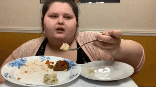 A Woman Is Eating A Plate Of Food With A Fork And Spoon GIF