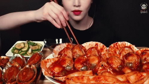 A Woman Is Eating A Plate Of Food With Chopsticks . GIF