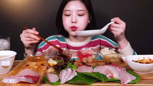A Woman Is Eating A Plate Of Food With Chopsticks And A Spoon GIF