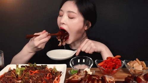 A Woman Is Eating A Plate Of Food With Chopsticks And A Spoon GIF