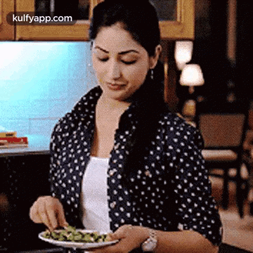 A Woman Is Eating A Salad In A Kitchen While Wearing A Watch . GIF