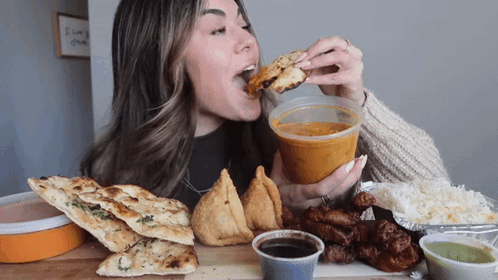 A Woman Is Eating A Sandwich And Holding A Cup Of Soup GIF