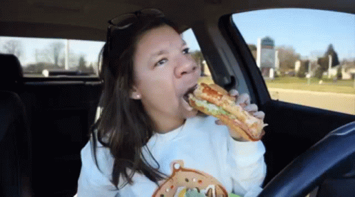 A Woman Is Eating A Sandwich In A Car . GIF