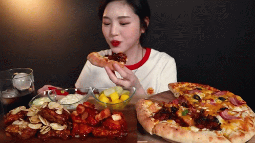 A Woman Is Eating A Slice Of Pizza Next To A Plate Of Food GIF
