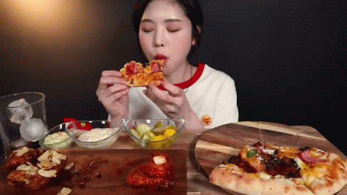 A Woman Is Eating A Slice Of Pizza Next To A Plate Of Pickles GIF