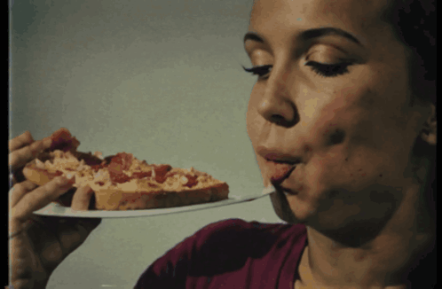 A Woman Is Eating A Slice Of Pizza With Her Tongue Out GIF