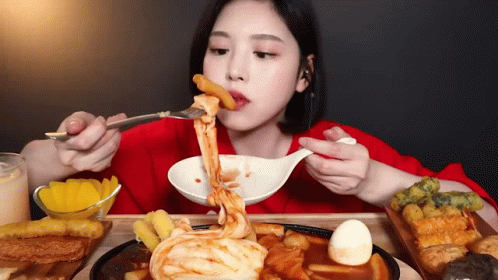 A Woman Is Eating Food With A Fork And Spoon . GIF