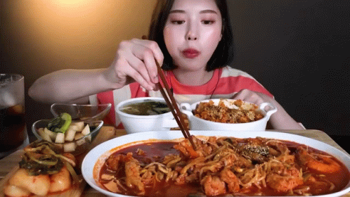 A Woman Is Eating Food With Chopsticks And A Bowl Of Soup GIF