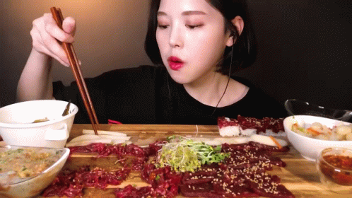 A Woman Is Eating Meat With Chopsticks While Wearing Ear Buds GIF