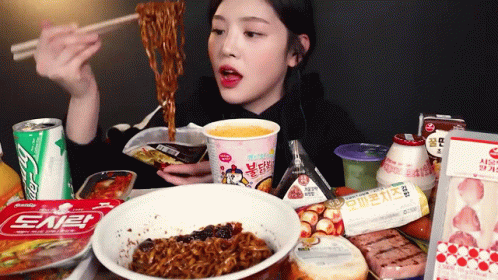 A Woman Is Eating Noodles With Chopsticks While Sitting At A Table Filled With Food . GIF