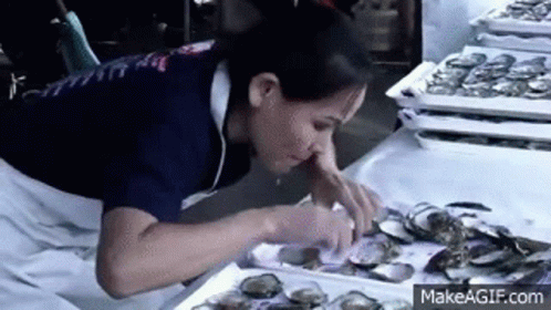 A Woman Is Eating Oysters At A Market . GIF