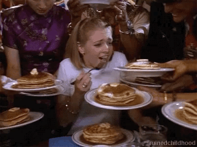 A Woman Is Eating Pancakes With A Fork While A Group Of People Are Holding Plates Of Pancakes . GIF