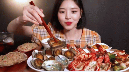 A Woman Is Eating Seafood With Chopsticks And A Spoon . GIF