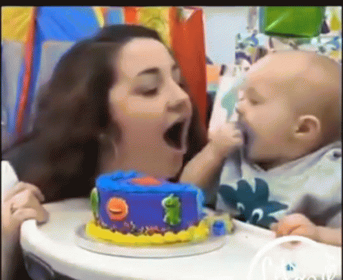 A Woman Is Feeding A Baby A Birthday Cake With A Frog On It . GIF