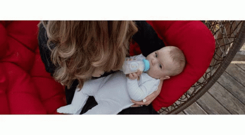A Woman Is Feeding A Baby From A Bottle While Sitting On A Red Chair . GIF