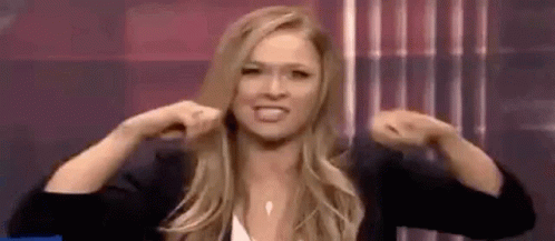 A Woman Is Flexing Her Muscles In Front Of A Curtain . GIF