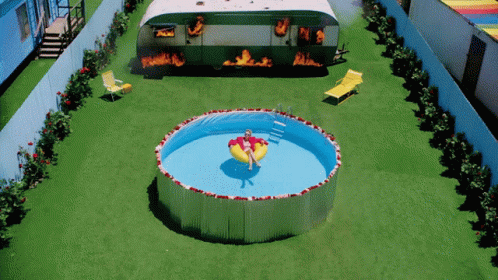 a woman is floating in a swimming pool in front of a trailer that is on fire